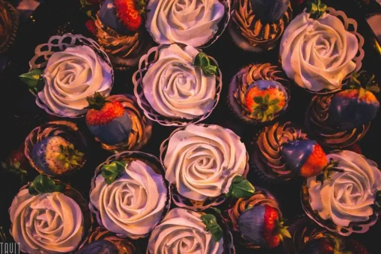 A close-up of cupcakes decorated with white rose-shaped frosting and chocolate-dipped strawberries, arranged in a visually appealing pattern—perfect for a seminar or corporate event dessert table.