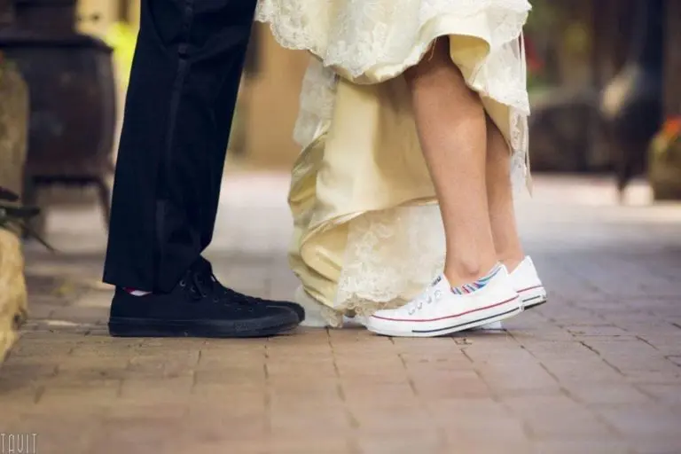 A bride in white sneakers and a wedding dress stands on tiptoe facing a groom in black dress pants and sneakers on a brick walkway, their faces hidden. It’s an unconventional style that could liven up any corporate event or seminar.