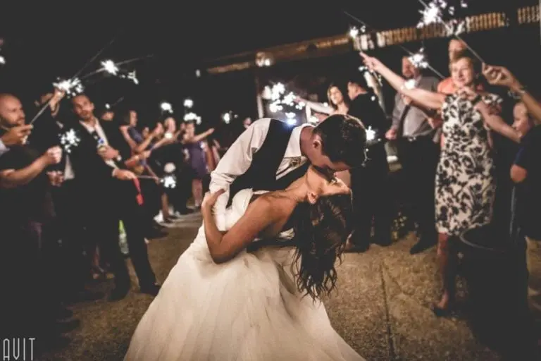 A bride and groom share a romantic kiss while dancing, surrounded by guests holding sparklers at night. The scene is festive and joyful, capturing a magical atmosphere unlike any seminar or corporate event.