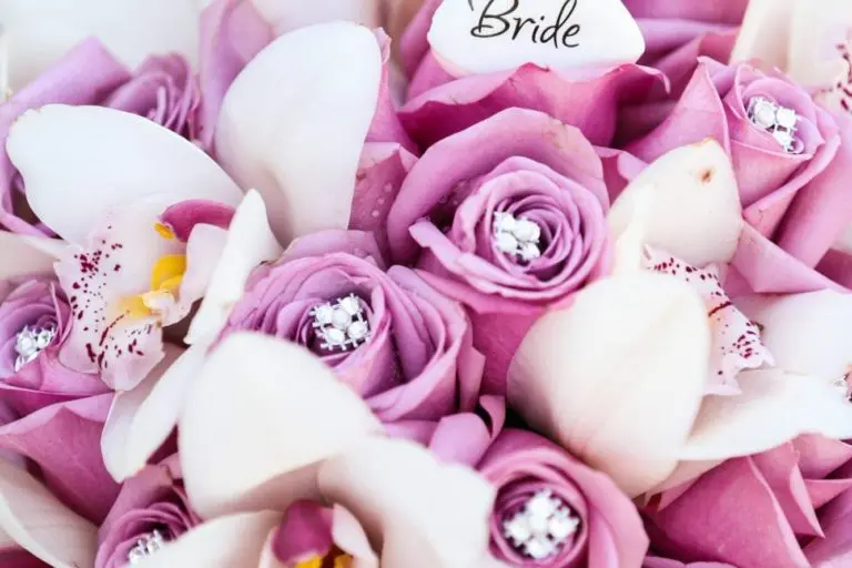 A bouquet of purple roses and white orchids with jeweled centers, perfect for event photography, featuring a small card labeled "Bride.