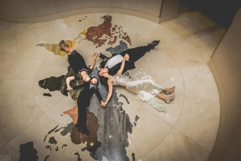 Four people dressed formally lie on their backs, holding hands in a star shape, on a large floor map of Scotland. The group is smiling and looking up at the camera, capturing a fun moment from their corporate event.