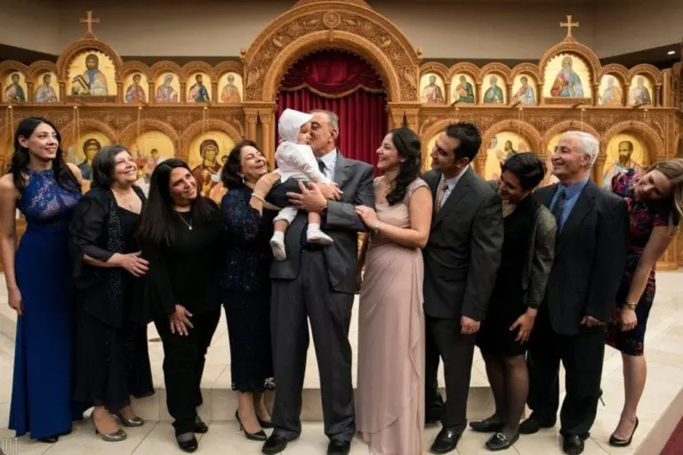 A group of people dressed formally pose and smile inside a church with ornate golden religious icons; a man at the center holds a baby as everyone looks at them affectionately, creating an atmosphere warmer than any seminar or corporate event.