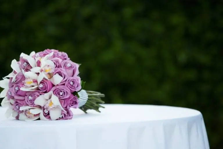 A stunning bouquet of pink roses and white flowers with jeweled accents graces a white table, perfect for enhancing any corporate event. The blurred green foliage backdrop adds a touch of elegance, beautifully captured in event photography.