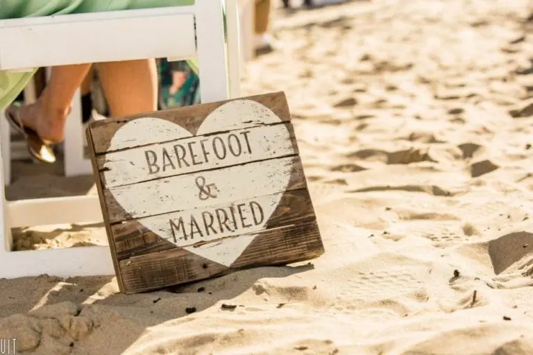 A wooden sign with a white heart and the words "Barefoot & Married" sits in the sand next to white chairs, adding charm to this beach wedding—perfect inspiration for a corporate event or seminar by the sea.