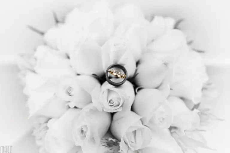 A close-up of white roses arranged in a bouquet with two wedding rings placed at the center, one gold and one silver with diamonds, making a striking focal point ideal for a corporate event or seminar celebrating lasting partnerships.