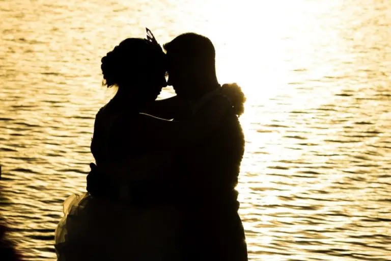 Silhouette of a bride and groom embracing by a lake at sunset, with sunlight reflecting off the water behind them—perfect for capturing the romance or elegance of a corporate event or seminar invitation.