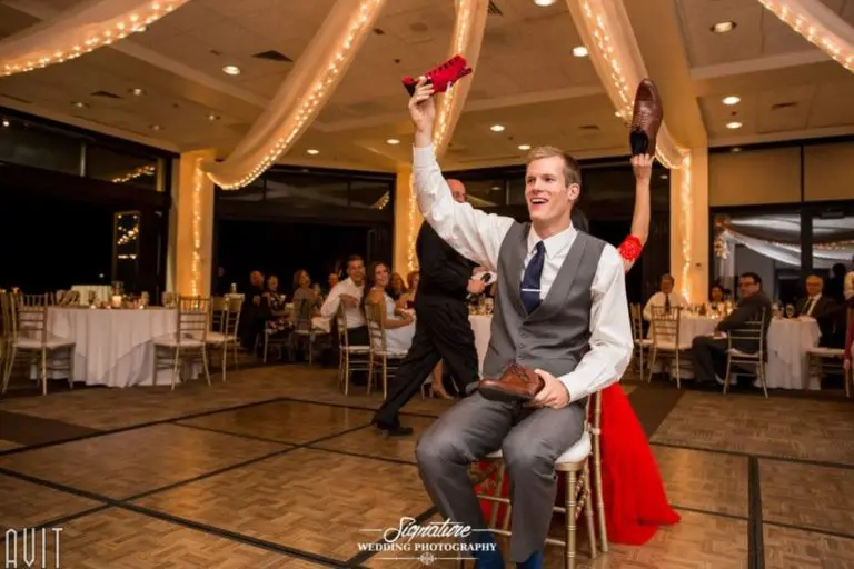 The bride and groom play the shoe game at their wedding reception, seated back-to-back on the dance floor under twinkling lights. Guests smile as they watch, much like attendees at a corporate event photography session capturing candid moments.