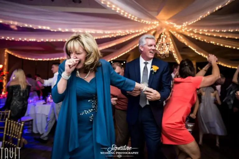 A joyous wedding reception scene with a woman in a blue dress and a man in a suit dancing, captured as if in professional headshots. Guests are energetically dancing in the background beneath twinkling draped lights, reminiscent of lively corporate event photography.