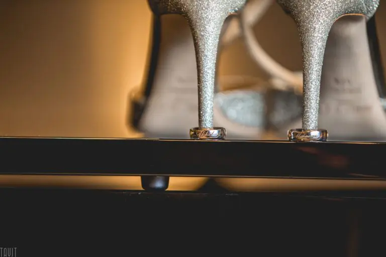 Close-up of two silver glitter high heels with wedding rings around the heels, resting on a glossy black surface—perfect for adding elegance to a corporate event or seminar, set against a warm, softly blurred background.