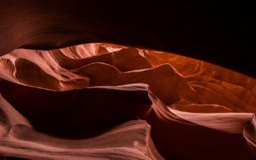 Sunlight streams into a narrow slot canyon, illuminating smooth, flowing rock formations in shades of orange and brown. Shadows accentuate the canyon’s curves—an inspiring scene reminiscent of a unique venue for a memorable corporate event.