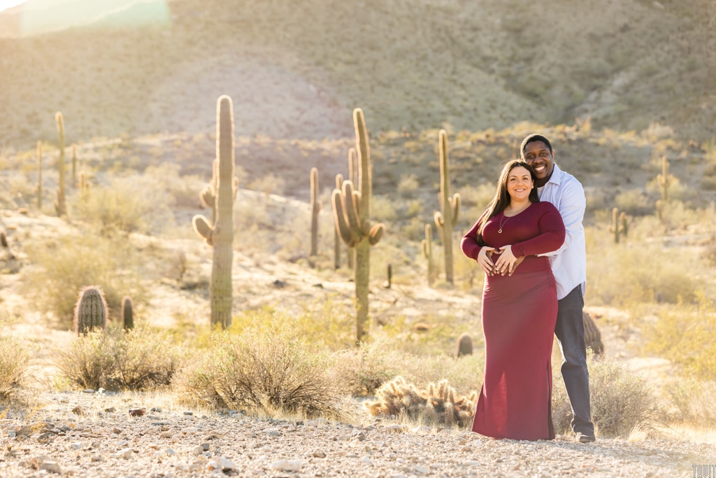 Couple smiling at camera in desert for maternity shoot