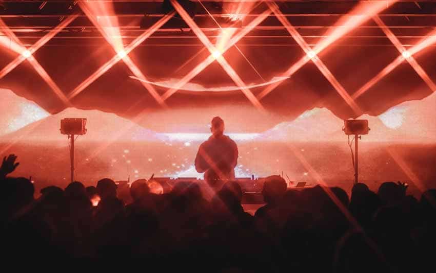 DJ on stage in front of crowd with red laser lights