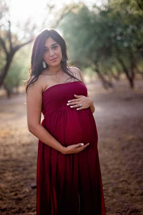 Woman in red dress in desert holding tummy maternity shoot