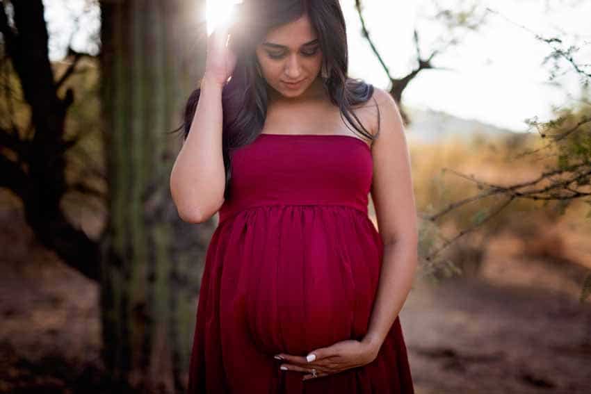 Woman in red dress looking down at pregnant tummy