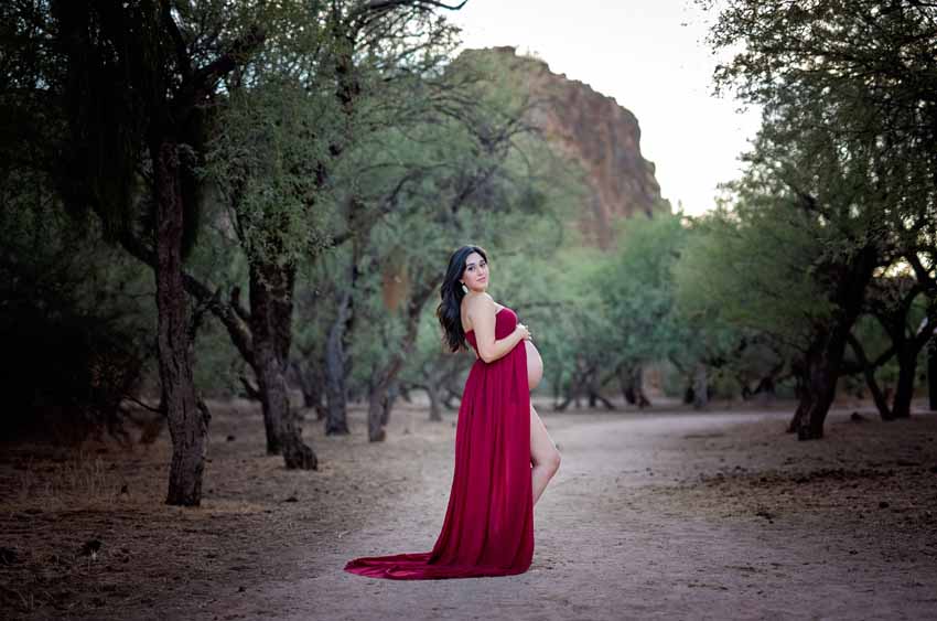 Woman in red dress in desert holding tummy maternity
