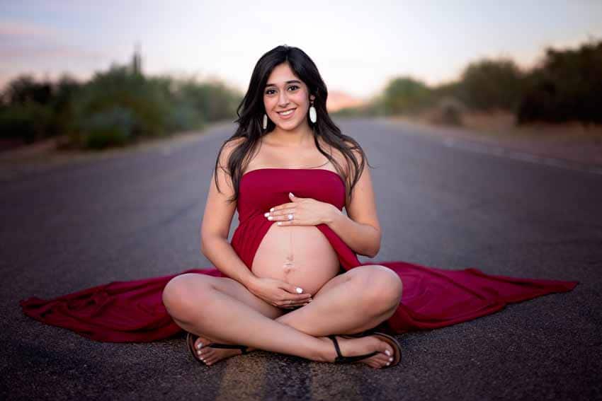 Woman in red dress sitting in road holding tummy maternity