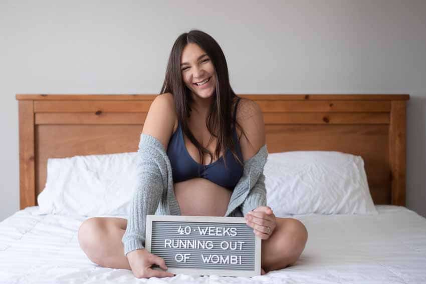 Pregnant woman sitting on bed with maternity sign
