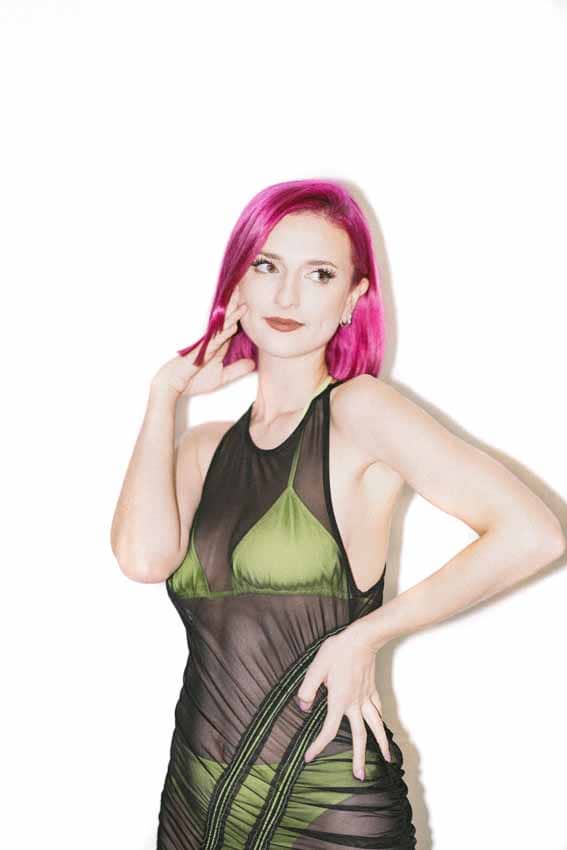 Woman with pink hair in green bathing suit with black mess cover over dress