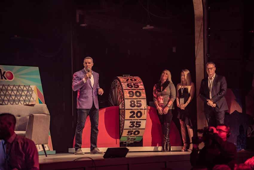 Group of people standing on stage next to number wheel