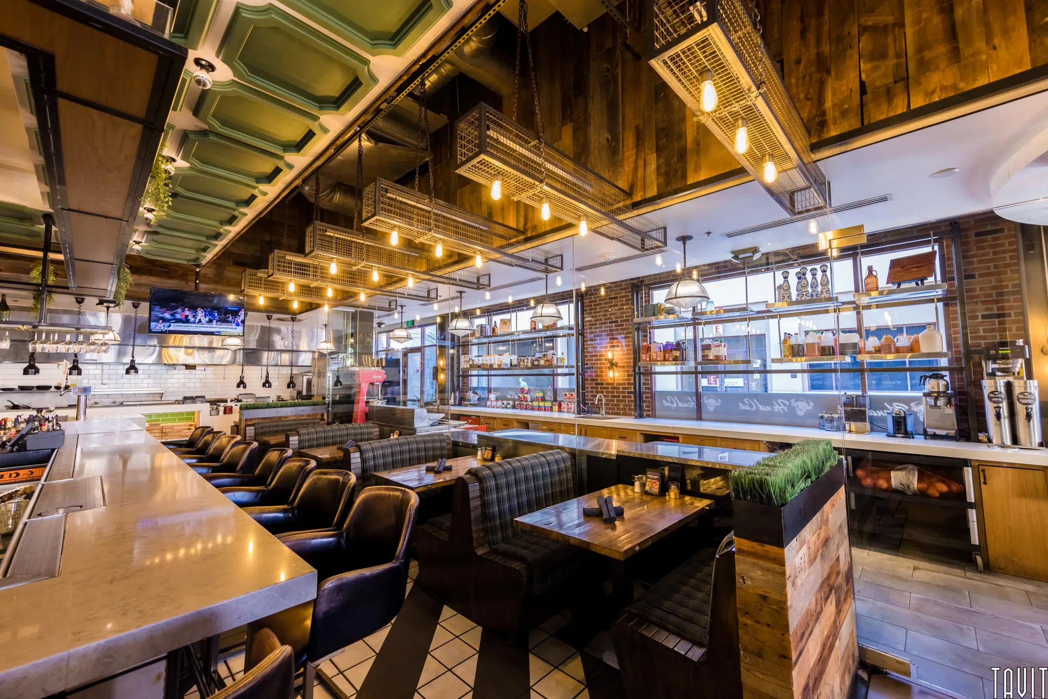 Modern restaurant interior with long marble bar, leather bar stools, cozy booth seating, and industrial accents—an inviting space ideal for a seminar or corporate event, featuring shelves of bottles, hanging lights, and stylish exposed ceiling fixtures.