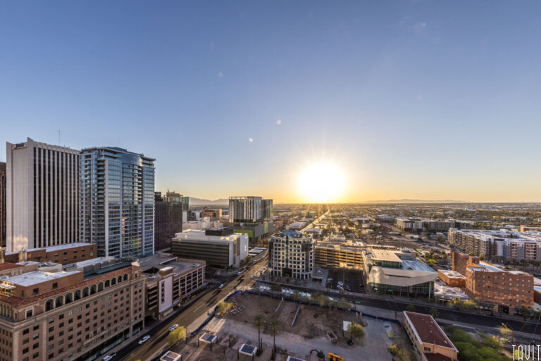 A cityscape at sunset with the sun low on the horizon, tall buildings on the left, shorter buildings and roads extending into the distance—a perfect backdrop for a seminar or corporate event under a clear sky.