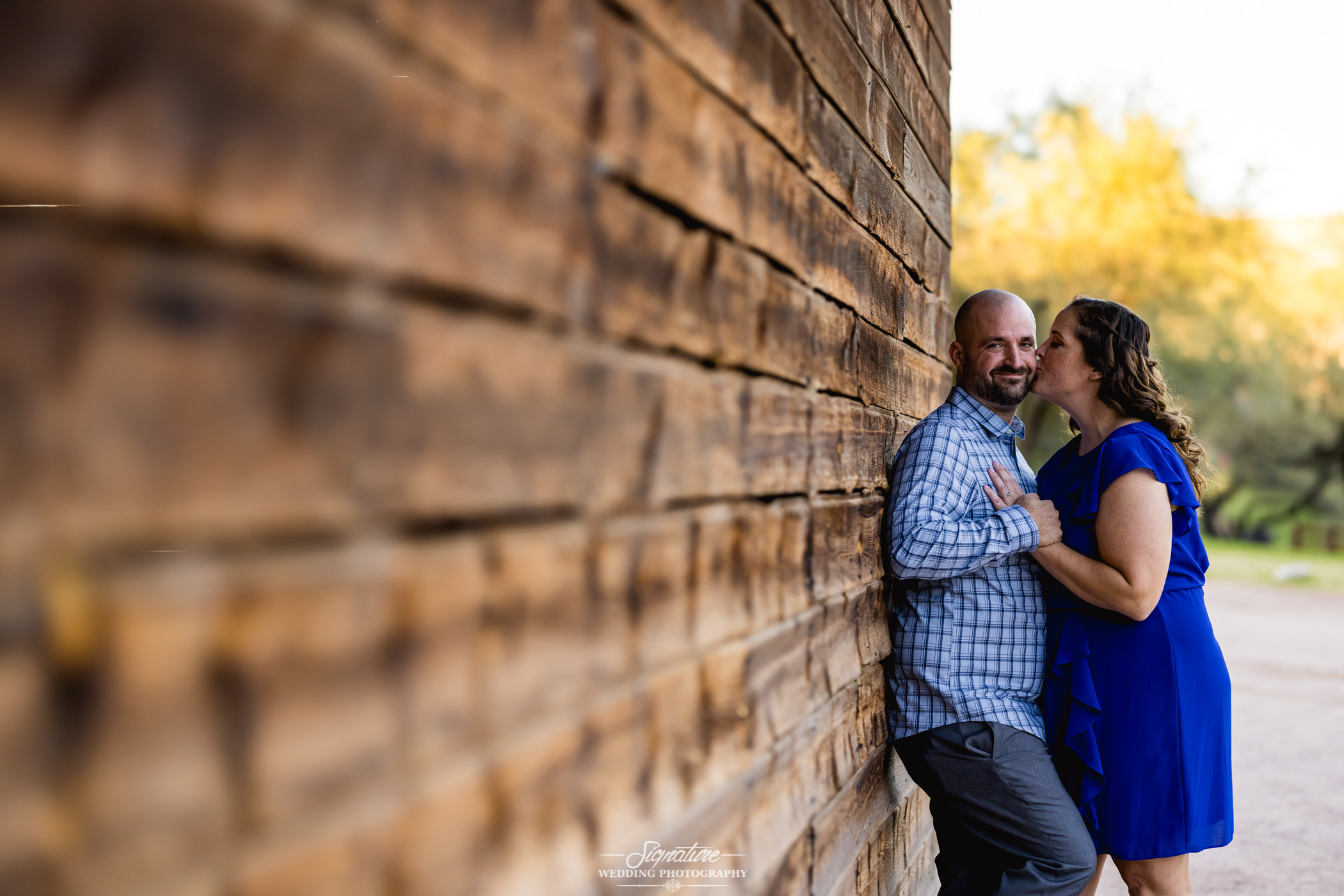 Woman kissing man's cheek against wooden barn