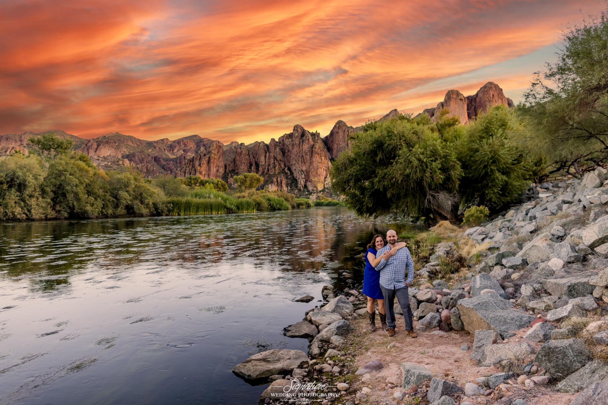 Woman hugging man's shoulders by creek at sunset