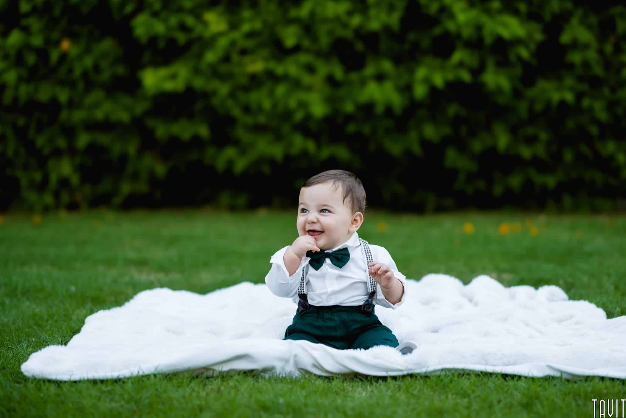 Baby sitting on blanket outside smiling