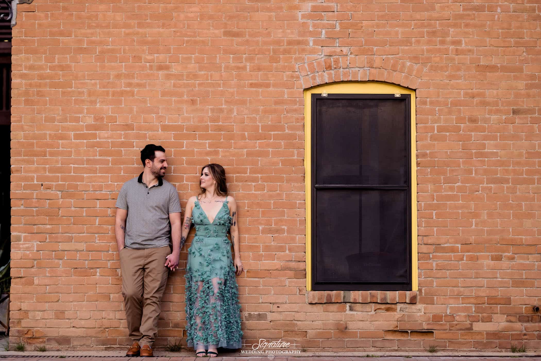 Couple holding hands with back against brick wall