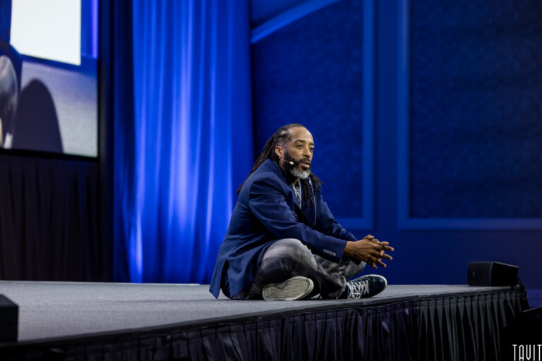 Man sitting on floor of stage giving presentation for business event