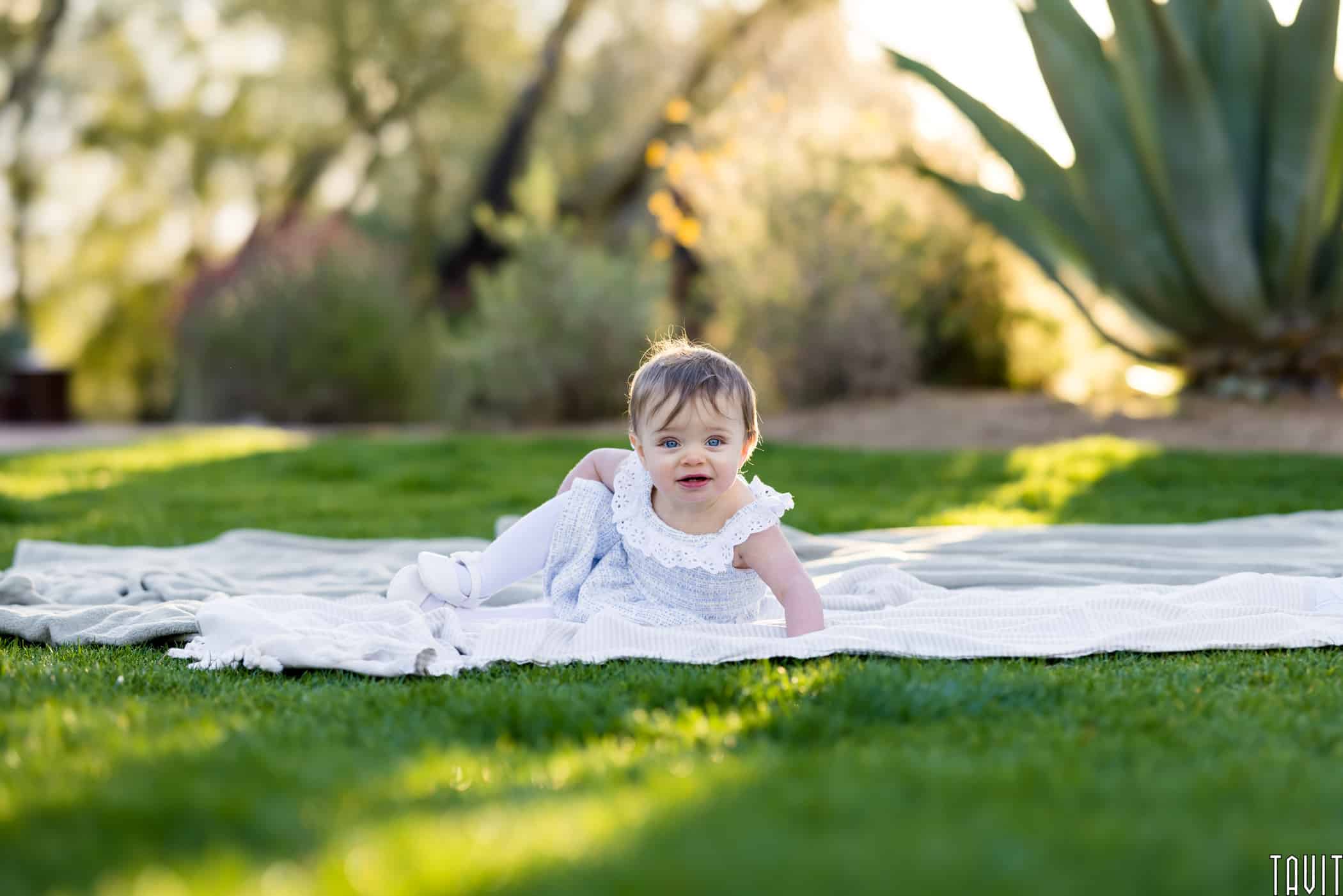 Baby sitting on white blanket outside
