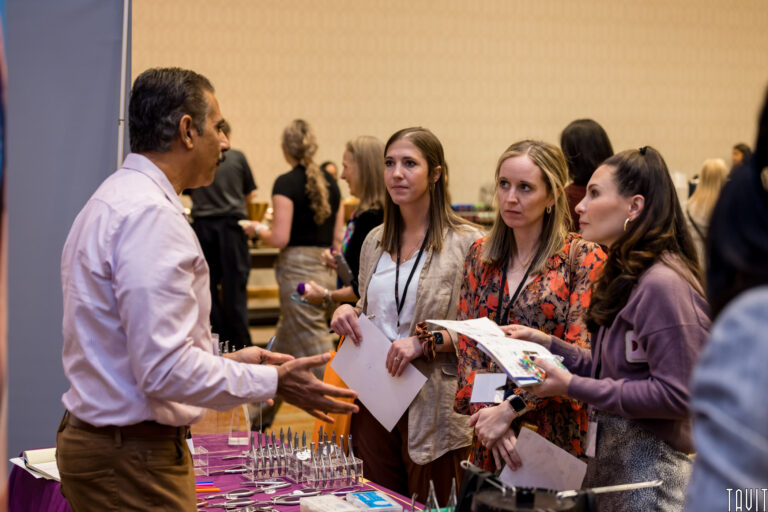 man at a booth talking to three women at a conference