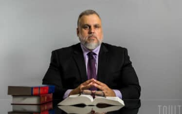 corporate headshot of man in business suit sitting at a table with books