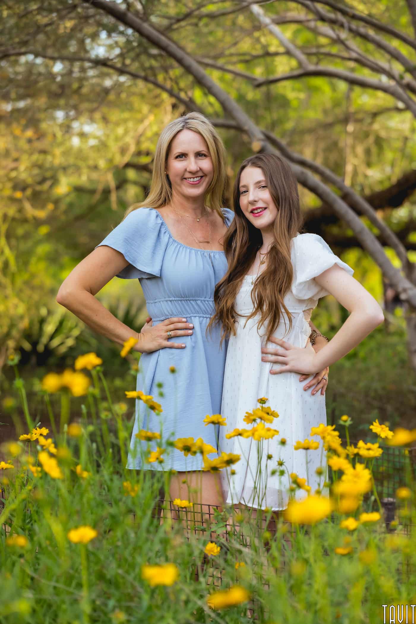 mom and daughter with flowers in front of them and trees behind them