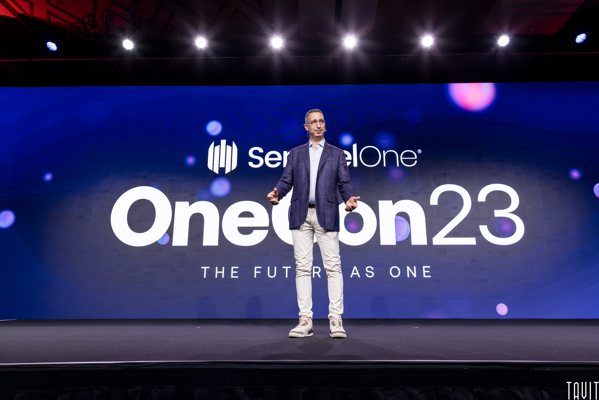 presenter standing on stage in front of SettinelOne's OneCon23 slide