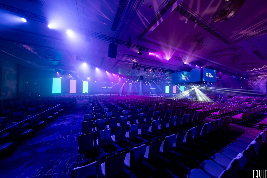 A large conference room filled with empty chairs faces a brightly lit stage with colorful lights and multiple screens, creating a dramatic effect—an ideal scene for an experienced Corporate Event Photographer Phoenix to capture professional event photography.