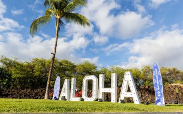 Large white marquee letters spell “ALOHA” under a palm tree and blue skies, with two blue event banners nearby. Perfect for Event Photography Phoenix or capturing memorable moments with a skilled Corporate Event Photographer.